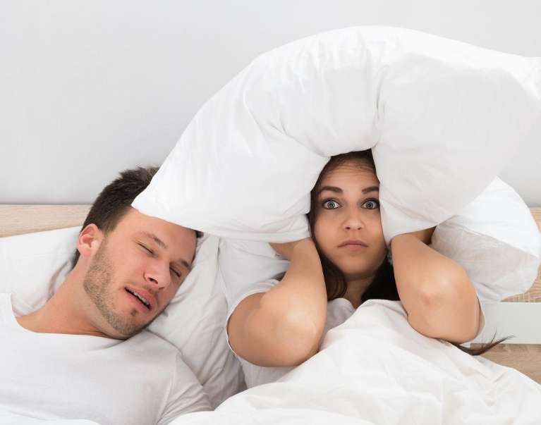An image showing a woman holding a pillow to her ears as her sleeping partner snore in Wahroonga