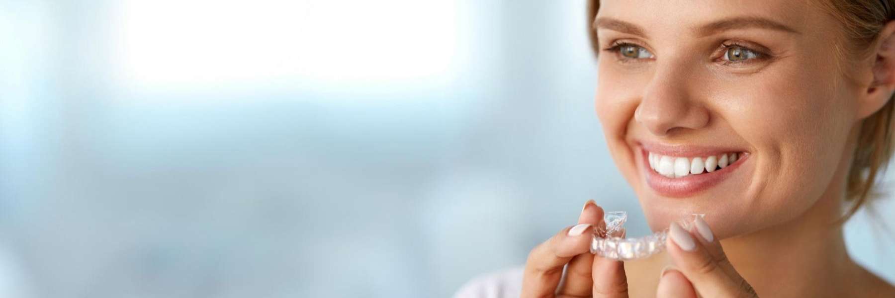 An image of a woman smiling while holding Invisalign® Clear Aligners in Wahroonga, NWS